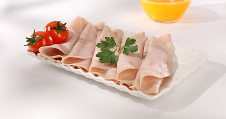 ham on a plate. meat delicacy with cherry tomato on a light background. turkey ham slices with parsley. cold appetizer on a white tablecloth. treat close-up.
