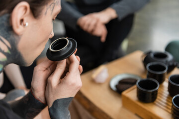 tattooed young man smelling puer tea near Chinese cups in yoga studio.