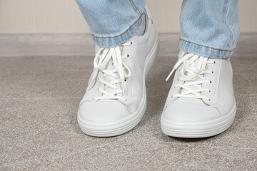Women's white leather sneakers on the legs indoors. Shoe care. Shoe laces and lacing