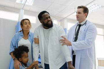 Doctors examine a black patient who has had an accident with a broken leg accompanied by his wife and child.