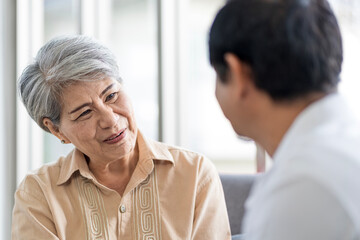 Obraz premium Asian couple, elderly man and woman sitting on the sofa having fun chatting together at home. Concept: health insurance, life insurance, retirement happiness.
