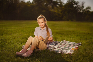 teenager girl holding book in hands and reading fiction sitting in green park