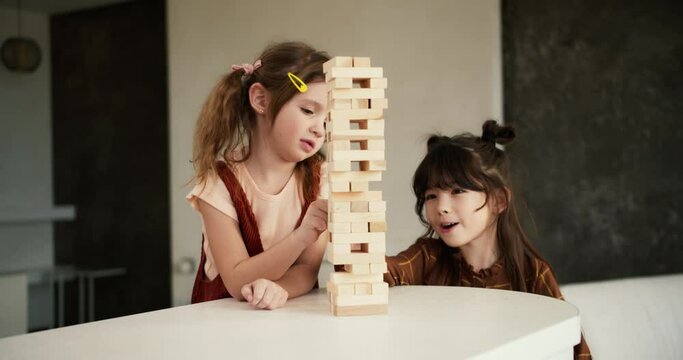 Two preteen girls friends children playing board game Jenga on table in kitchen at home