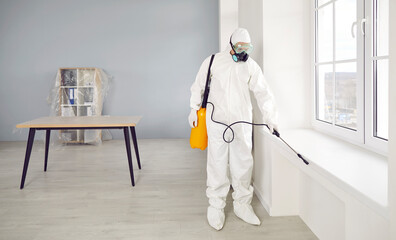 Man wearing protective ppe suit, glasses and face mask disinfecting office workspace during...