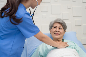 A female nurse or doctor is caring for an elderly female patient lying on the patient's bed doing heart and breathing tests. and the patient has a smile