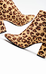 Feminine and sexy vogue fashion style. A creative close-up of elegant heeled boots with a leopard pattern. The white background and animalistic print create a modern daring design of the photo.