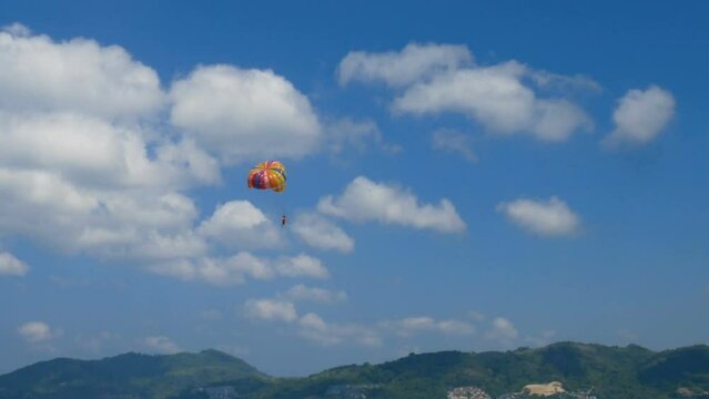 excited tourists hanging on parasailing flying high in the sky, outdoor extreme sport summer activity. colorful parachute on blue sky background