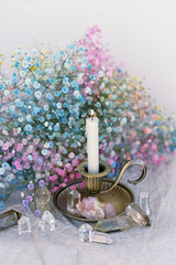 crystals, candlestick and flowers on table close up, blurred light background. Magic esoteric...