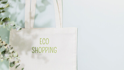 Fototapeta na wymiar Sustainable shopping, buying or sales concept. Eco friendly still life with white textile shopping bag with text Eco shopping on blue background with plant shadows. Flat lay, copy space