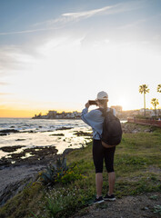 Rear view of a woman dressed in spring clothing taking pictures of a coastal village at sunset in Spain.