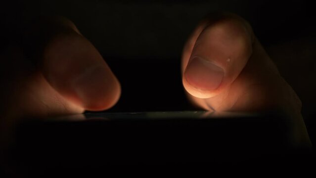 Using a smartphone in the dark. Male fingers touch the gadget screen. There is only one light source