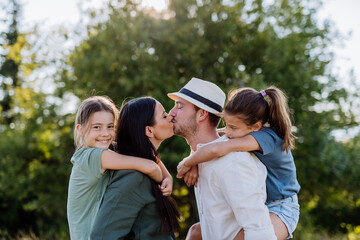 Portrait of young couple with their daughters in the nature, kissing. Side view.
