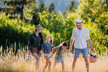 Happy young parents with daughters walking for picnic in nature in summer day,