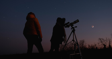Two amateur astronomers looking at stars, planets and Moon with astronomy telescope outdoors.