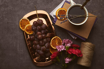 Aesthetic fine art breakfast with grapes, cup of coffee, dry oranges, books and flowers on the golden tray