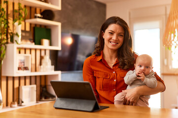 Portrait of a pretty mother and her cute little baby girl at home with a tablet on the stand.