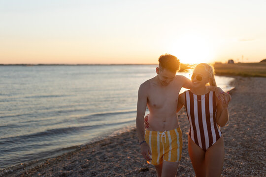 Happy young couple in striped swimsuits walking in the beach during sunset. - Powered by Adobe