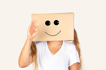 Mujer con caja de cartón en la cabeza con gesto positivo y feliz  haciendo el gesto de ok sobre fondo blanco liso y aislado. Vista de frente y de cerca. Copy space