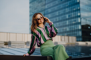 Portrait of beautiful young woman with smartphone outdoor in city, during sunset.