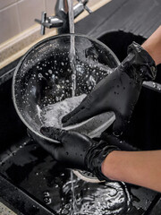Washing dishes. Hands in nitrile, rubber gloves. Transparent bowl, salad bowl, in foam, under running water. Tap water, sponge, dish detergent. Cleaner, sink, kitchen sink. Disposable gloves.