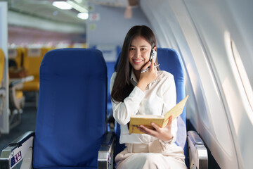 Asian business woman passenger sitting on business class luxury plane while working using smart phone mobile talking and use notebook while travel concept