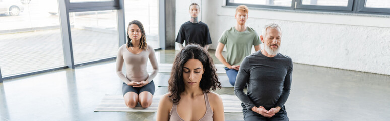 Multicultural people meditating in Thunderbolt asana on yoga mats in studio, banner.