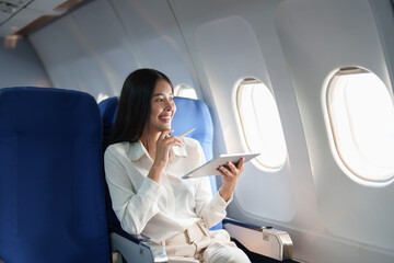 Asian attractive business woman passenger sitting on business class luxury plane while tablet...