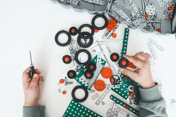 A little boy with a screwdriver in his hands plays with a metal constructor