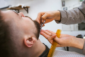A barber is working on a client's beard.