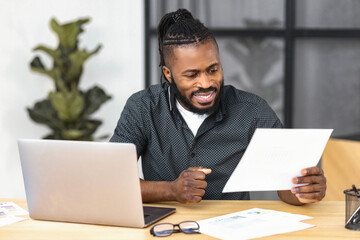 Successful male entrepreneur or CEO, investor or financier looking through a report, working with documents and accounts smiling satisfied with work results andachievements sitting in modern office