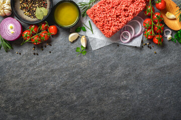 Ingredients for cooking. Food background with fresh minced meat, spices, olive oil and vegetables on dark background top view, recipe and menu concept