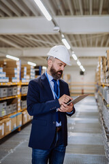 Manager in suit controlling goods in a waehouse.