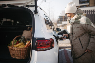 Close up of senior woman charging electric car.