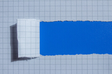 Fototapeta premium Graph paper torn on a blue background. Ripped checkered paper with copy space.