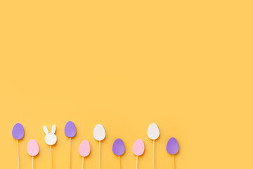 Easter frame composition with minimal style eggs and rabbit wood toys on pastel light yellow background. Trendy composition, holiday concept. Flat lay, top view, place for text, card