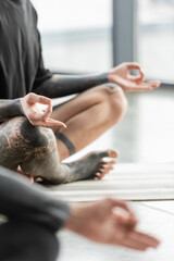 Cropped view of tattooed man practicing gyan mudra in yoga class.