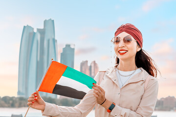 Indian girl with UAE flag against scenic skyscrapers in Abu Dhabi. Immigration, student education...