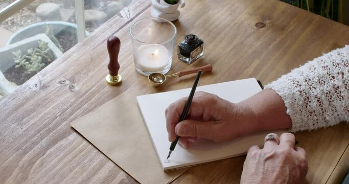 A person is hand writing a letter to a friend using a quill pen, inkwell, and vintage stationary.