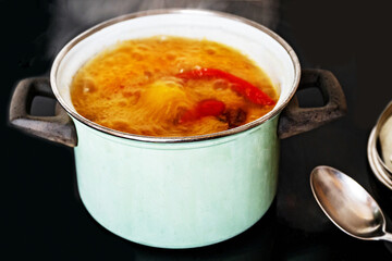 Boiling and bubbling soup from pepper and tomato in green pot on hob.
