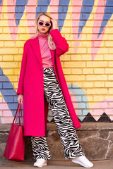 Fashionable confident blonde woman wearing trendy pink sunglasses, fuchsia color midi coat, ...