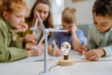 Young teacher with model of wind turbine learning pupils about wind energy.
