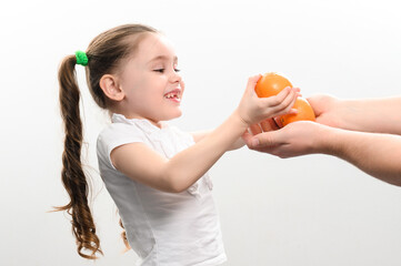 A little girl is given tangerines on a white background, the child takes tangerines.