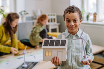 Little boy posing with model of wind turbine and model of house with solar system during a school lesson. © Halfpoint
