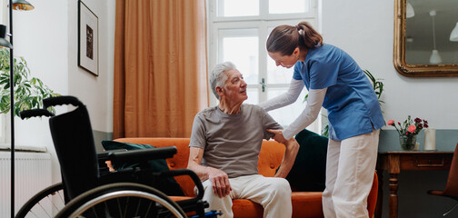 Young nurse helping senior man to stand up.