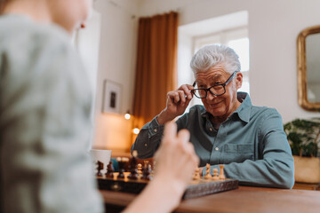 Senior man playing chess with his granddaughter.