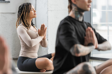 Young african american woman doing anjali mudra in yoga group.