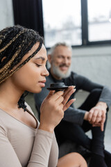 young african american woman with dreadlocks smelling puer tea near middle aged man on blurred background.