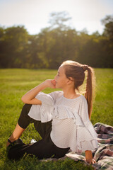 dreaming teenage girl in casual clothes resting in green park, sitting on green grass and looking at the distance