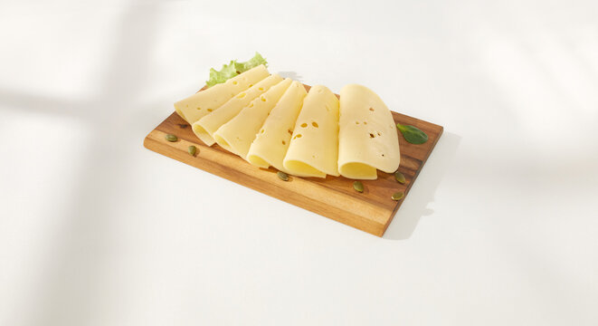 slices of cheese with herbs on a wooden board. maasdam on a light background. yellow cheese under sunlight. dairy products on the table