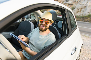 Naklejka premium Bearded man using digital tablet inside car while travel and road trip vacation holidays - road map and navigation concept